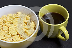 Useful breakfast. Corn sticks flakes in a container and a mug of coffee. On a dark background.
