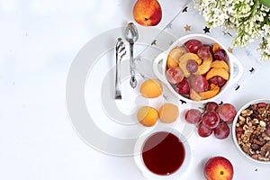 Useful breakfast, food for children, fruit salad with peaches, pears, granola, grapes and flower tea on a bright table. The