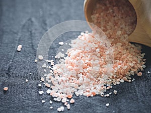 Useful spices concept. Large dark pink himalayan salt spilled from a wooden cup onto a black tablecloth. Closeup