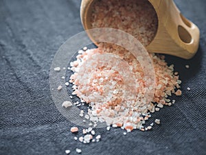 Useful spices concept. Large dark pink himalayan salt spilled from a wooden cup onto a black tablecloth. Closeup