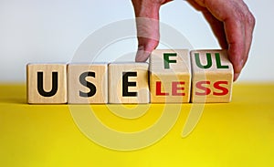 Useful or useless symbol. Male hand turns cubes and changes the word `useless` to `useful`. Beautiful yellow table, white