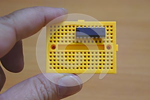 A user holding a yellow protoboard horizontally with an ic mounted