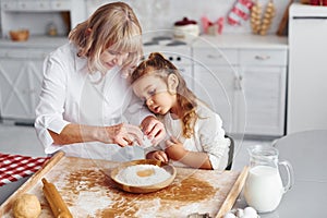 Uses eggs. Senior grandmother with her little granddaughter cooks sweets for Christmas on the kitchen