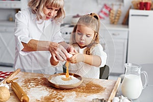 Uses eggs. Senior grandmother with her little granddaughter cooks sweets for Christmas on the kitchen