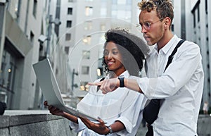 Uses laptop. Man with afrian american woman together in the city outdoors