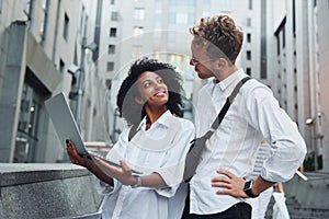 Uses laptop. Man with afrian american woman together in the city outdoors