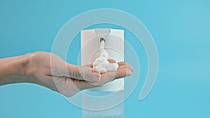 Using an automatic soap dispenser. Young girl woman brings her hands to dispenser on blue background. Concept of hand