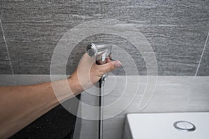 Using of bidet shower in bathroom with a bidet or toiler. Bidet shower in male hand for using it in a bathroom.