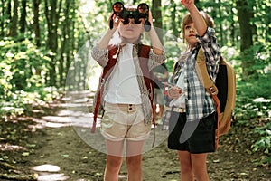 Using binoculars. Kids in forest at summer daytime together