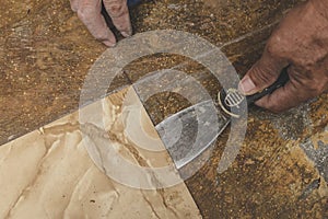 Using a blade scrapper or putty knife to remove old vinyl tiles from the floor. Home renovation concept