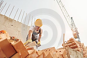 Using bricks. Young construction worker in uniform is busy at the unfinished building