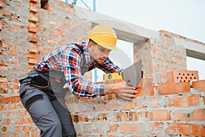 Using bricks. Young construction worker in uniform is busy at the unfinished building