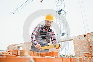 Using bricks. Young construction worker in uniform is busy at the unfinished building