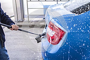 Using a brush to wash a car on a car washing facility on sunny summer day.Manual car wash with pressurized water in car wash