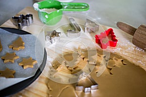 Making homemade festive Christmas cookies using cookie cutters and dough rolled out on a wooden pastryboard