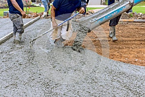 Using a concrete mixing truck, workers poured wet cement onto driveway of new house