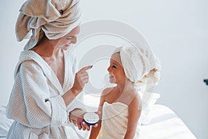 Using cream to clear skin. Young mother with her daugher have beauty day indoors in white room