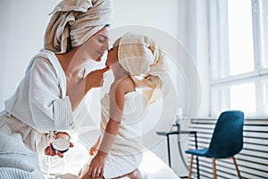 Using cream to clear skin. Young mother with her daugher have beauty day indoors in white room