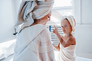 Using cream to clear skin. Young mother with her daugher have beauty day indoors in white room