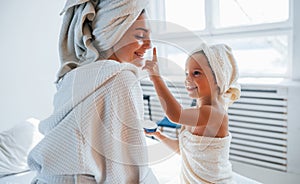 Using cream to clear skin. Young mother with her daugher have beauty day indoors in white room