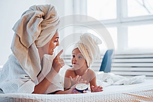 Using cream. Young mother with her daugher have beauty day indoors in white room