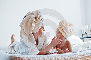 Using cream. Young mother with her daugher have beauty day indoors in white room