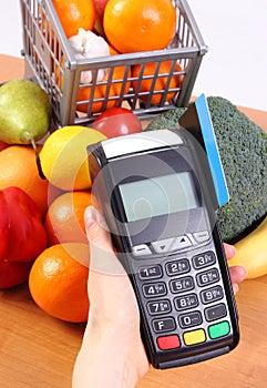 Payment terminal with credit card and fresh fruits and vegetables, cashless paying for shopping