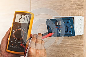 Using a digital meter to measure the voltage at an electric outlet socket box