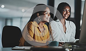 Using the extra hours to beat some deadlines. two young businesswomen working together on a computer in an office at