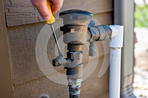 Using a flathead screwdriver to close the test cock next to the vacuum breaker to startup a sprinkler irrigation system in the