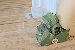 Using a floor sander carpenter grinds wood parquet floors in new house that has just been built