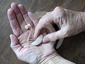 Using a hearing aid as a result of worsened hearing impairment. Hands hold hearing device photo