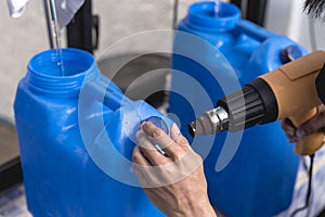 Using a heat gun to tighten the plastic seal on the cap lid of a blue 20 liter HPDE water container. A purified water refilling