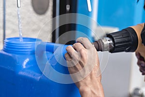 Using a heat gun to tighten the plastic seal on the cap lid of a blue 20 liter HPDE water container. A purified water refilling