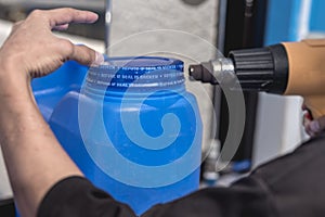 Using a heat gun to tighten the plastic seal on the lid of a blue 20 liter HPDE water container. A purified water refilling