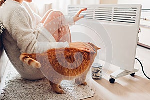 Using heater at home in winter. Woman warming her hands with cat. Heating season