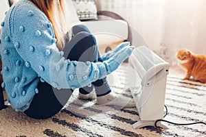 Using heater at home in winter. Woman warming her hands with cat wearing sweater. Heating season