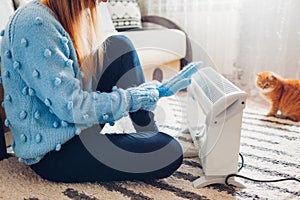 Using heater at home in winter. Woman warming her hands with cat wearing sweater. Heating season