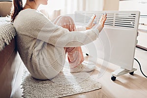 Using heater at home in winter. Woman warming her hands. Heating season.