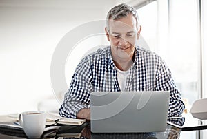 Using his bit of free time to do some browsing. a mature man working on a laptop at home.
