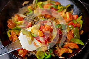 Using iron pan stir-fry tomatoes and bell peppers.