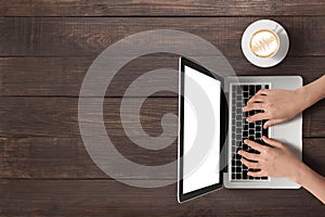 Using laptop and a cup of coffee on wooden background