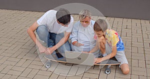 Using laptop on longboard while sitting sidewalk. Modern communication of youth