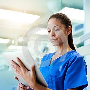 Using the latest technology to her patients benefit. a young nurse using a tablet while standing inside a clinic.