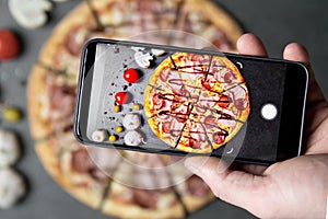 Using mobile phone to photograph the Pizza . Pizza with ingredients on a stone table top view