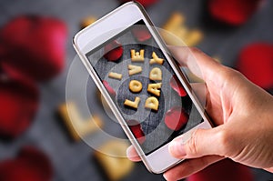 Using mobile phone to take photos of Cookies ABC in the form of word I LOVE DADY alphabet with red rose petal on old jean