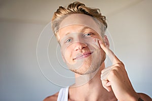 Using moisturizer will make a world of difference. a young man applying moisturizer to his face.