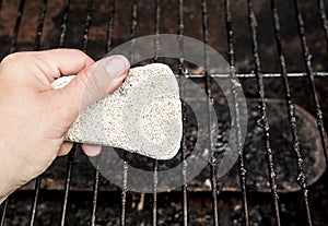 Using natural pumice stone to scrub charred food deposits and rust from BBQ grill metal grid.