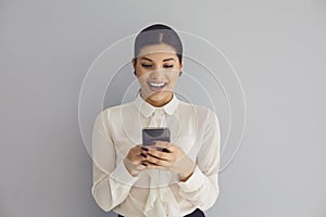 Using the phone on social networks. Hispanic young happy woman typing sms in mobile smiling while standing on gray