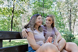 Using a smartphone.Mom and her teenage daughter have fun laughing on a walk in a summer park.
